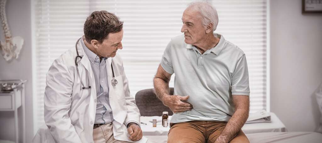 Senior man showing stomach ache pain to doctor